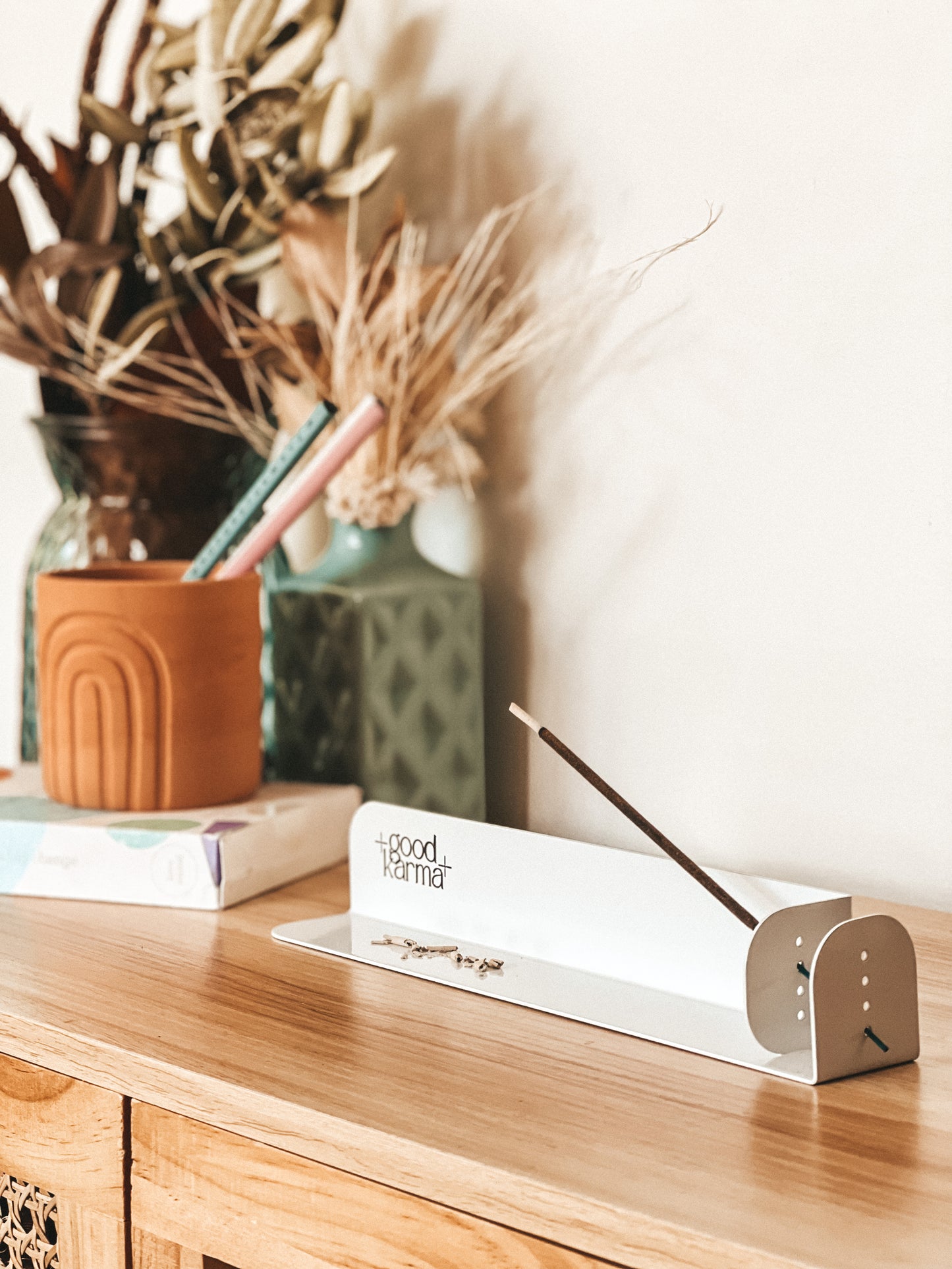 white metal incense sticks holder incense burner with one incense stick on the table with flowers on the background