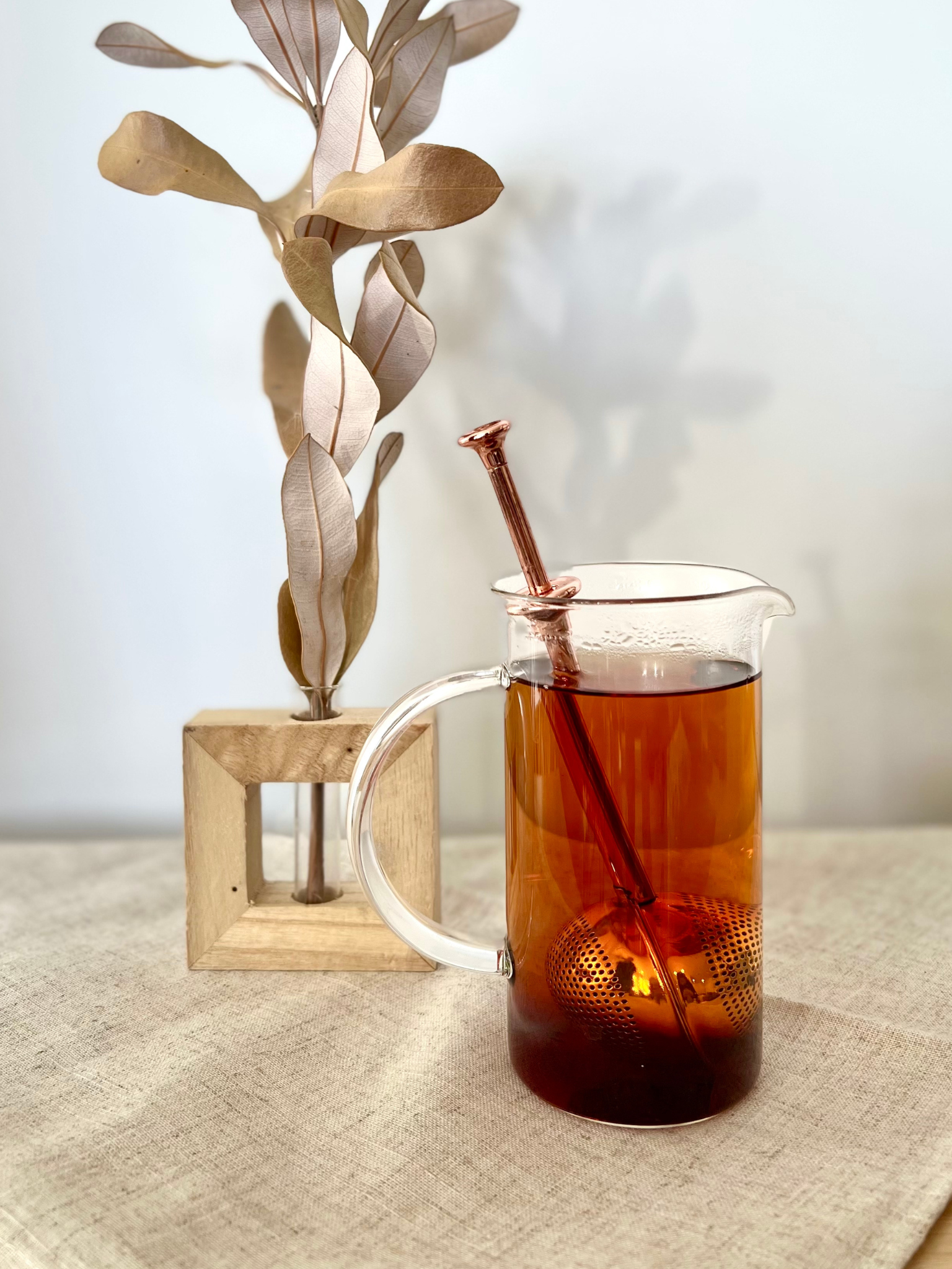 Good Karma tea infuser ball is 2-in-1 scoop and a strainer rose gold color inside transparent cup of tea and vase with flower